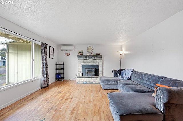 living room with a wall unit AC, a wood stove, a textured ceiling, and hardwood / wood-style flooring