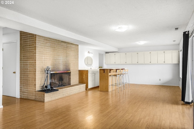 unfurnished living room with a textured ceiling, light wood-type flooring, and a brick fireplace