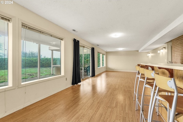 spare room with plenty of natural light, light hardwood / wood-style floors, a textured ceiling, and bar area