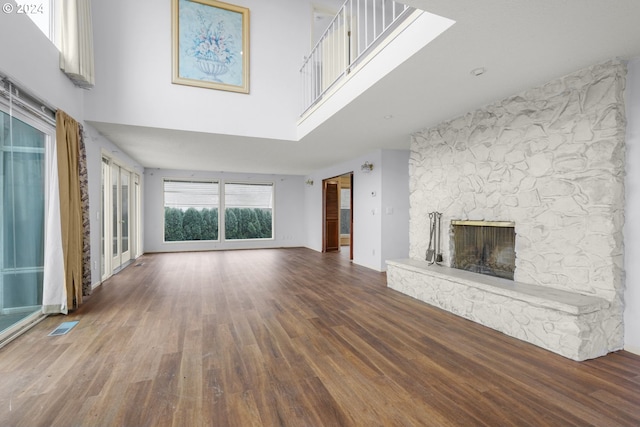 unfurnished living room featuring a stone fireplace, dark wood-type flooring, and a high ceiling