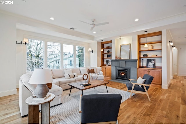 living room featuring baseboards, built in features, a lit fireplace, light wood-style floors, and recessed lighting