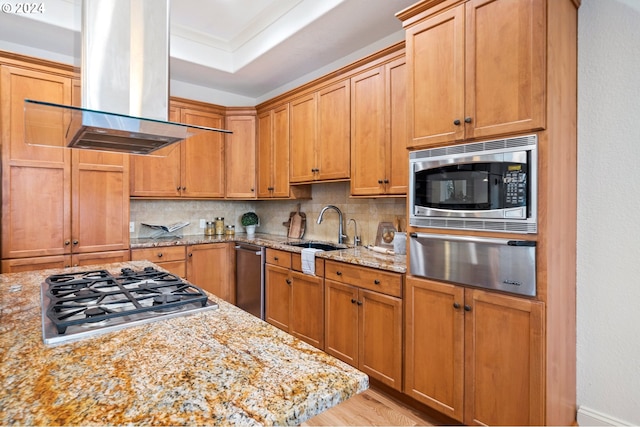 kitchen with decorative backsplash, light stone counters, island exhaust hood, stainless steel appliances, and a sink