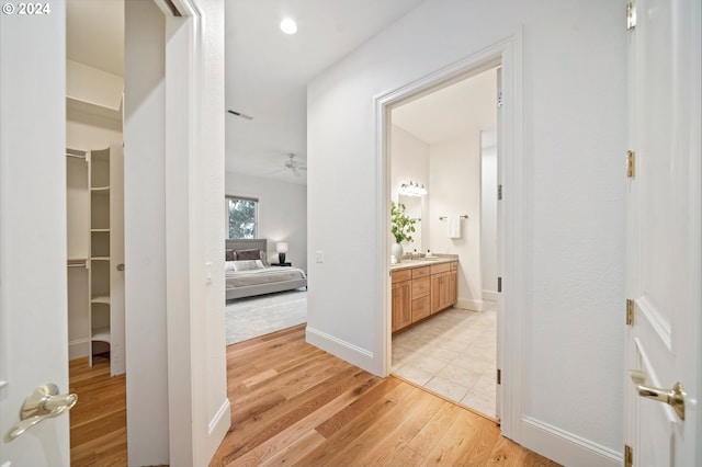 hallway with visible vents, a sink, light wood-style flooring, and baseboards