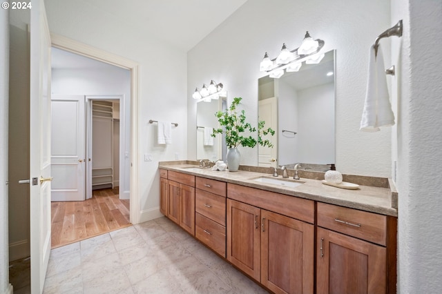 bathroom featuring a sink, double vanity, a walk in closet, and baseboards