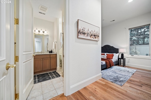 hallway with light wood finished floors, a sink, visible vents, and baseboards