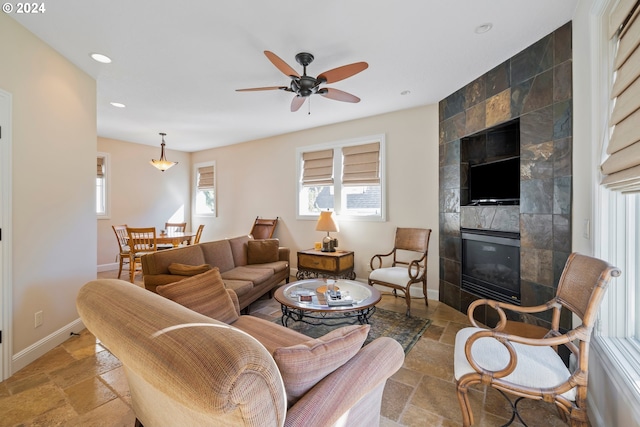 living area with recessed lighting, stone tile flooring, ceiling fan, a tile fireplace, and baseboards