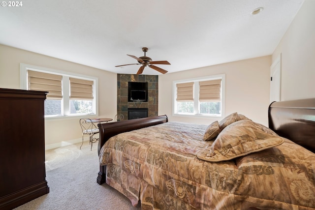 bedroom featuring light carpet, ceiling fan, baseboards, and a tiled fireplace