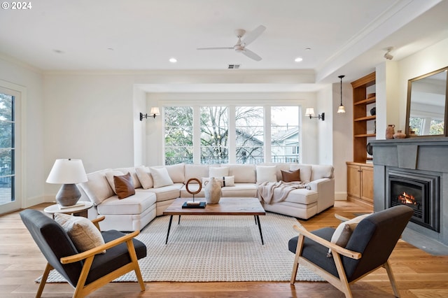 living room with recessed lighting, visible vents, light wood-style floors, a glass covered fireplace, and crown molding