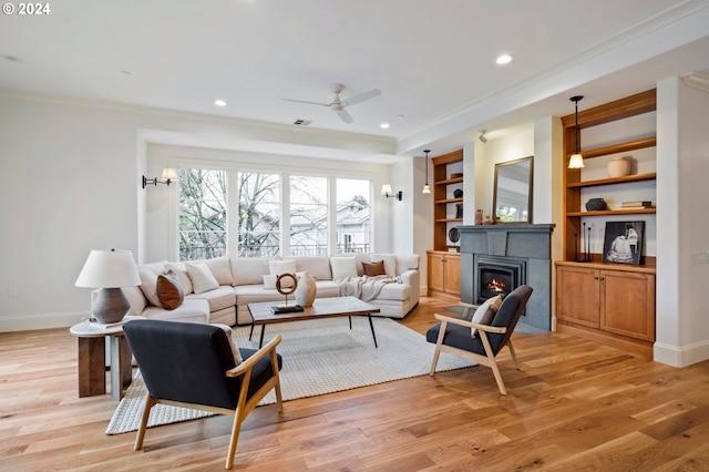 living area with baseboards, ornamental molding, a glass covered fireplace, and light wood-style floors