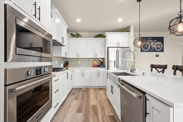 kitchen with white cabinets, light hardwood / wood-style flooring, sink, decorative light fixtures, and stainless steel appliances