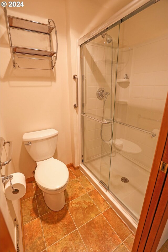 bathroom with a shower with door, toilet, and tile patterned flooring