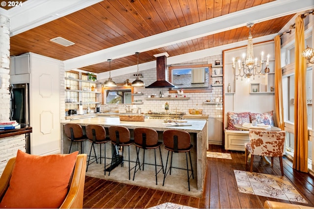 kitchen with wall chimney exhaust hood, a healthy amount of sunlight, dark hardwood / wood-style flooring, decorative light fixtures, and a breakfast bar