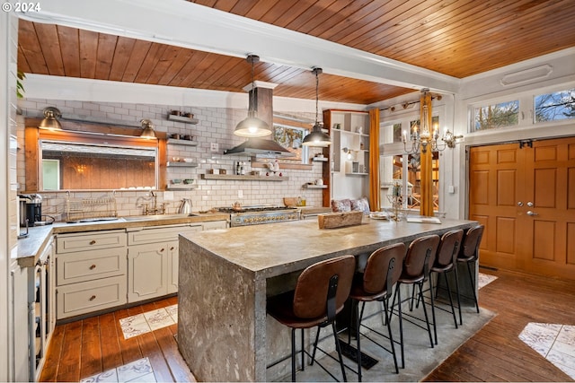 kitchen with sink, hanging light fixtures, dark wood-type flooring, wall chimney range hood, and a breakfast bar