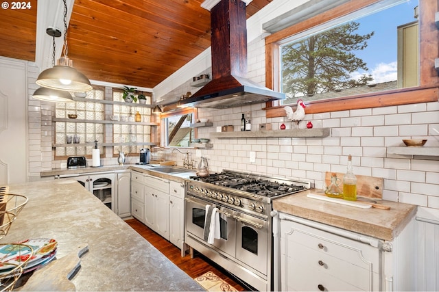 kitchen featuring pendant lighting, double oven range, wall chimney range hood, sink, and white cabinetry