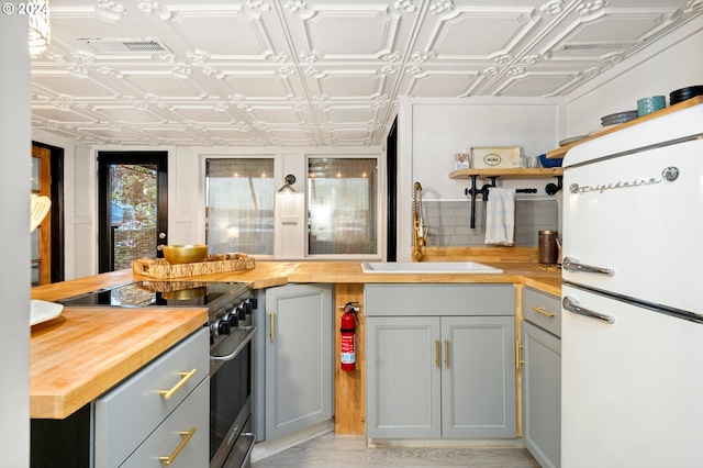 kitchen with wooden counters, white refrigerator, sink, high end stainless steel range oven, and gray cabinets