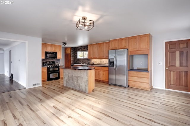 kitchen with decorative backsplash, light wood-type flooring, black appliances, sink, and a center island