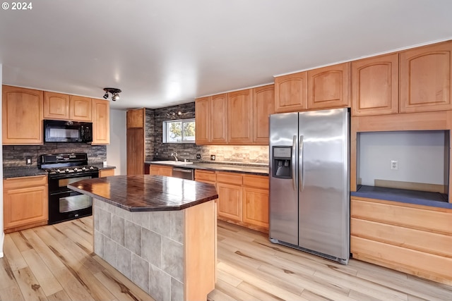 kitchen with sink, light hardwood / wood-style floors, black appliances, and a center island