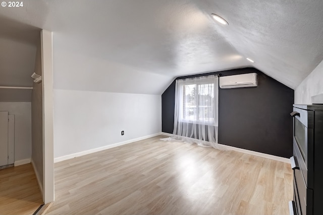 bonus room with an AC wall unit, vaulted ceiling, and light wood-type flooring