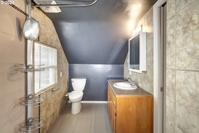 bathroom featuring toilet, tile patterned floors, tile walls, vaulted ceiling, and vanity