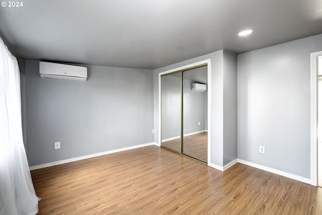 unfurnished bedroom featuring a wall mounted AC, light hardwood / wood-style flooring, and a closet