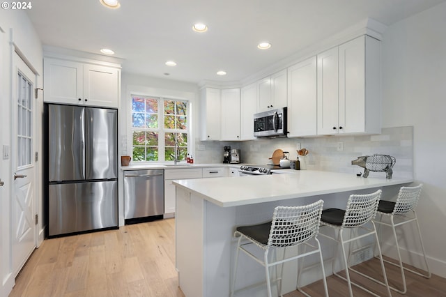 kitchen featuring light wood-type flooring, kitchen peninsula, white cabinetry, stainless steel appliances, and a breakfast bar