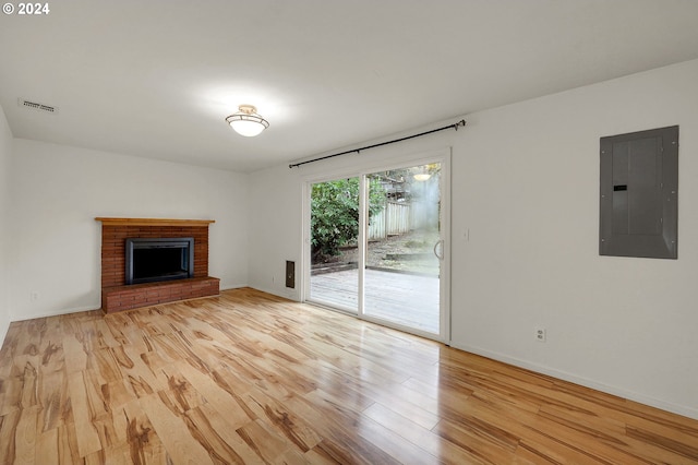 unfurnished living room with electric panel, light hardwood / wood-style floors, and a brick fireplace