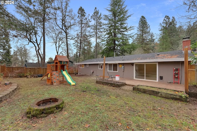 rear view of property featuring a fire pit, a playground, and a yard