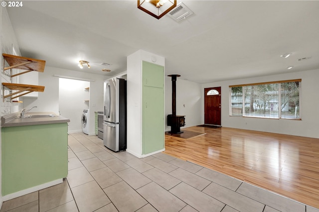 kitchen with light wood-type flooring, sink, washing machine and clothes dryer, a wood stove, and stainless steel refrigerator