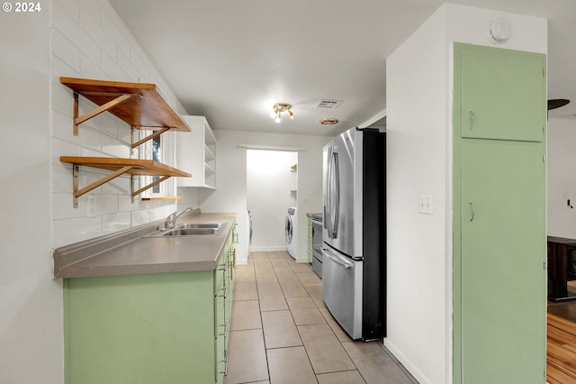 kitchen with decorative backsplash, stainless steel fridge, washer and clothes dryer, sink, and light tile patterned floors