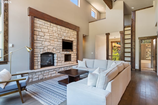 living room featuring a stone fireplace, a towering ceiling, and dark wood-type flooring