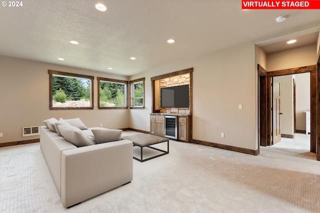 living room featuring bar, light colored carpet, a textured ceiling, and beverage cooler