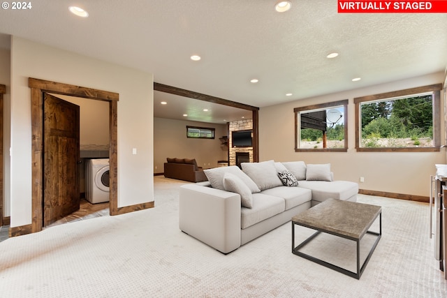 living room featuring a textured ceiling, a stone fireplace, light colored carpet, and washer / dryer