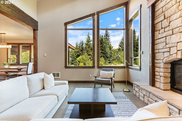 living room featuring beamed ceiling, hardwood / wood-style floors, a textured ceiling, and a stone fireplace