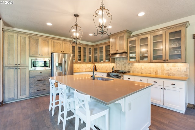 kitchen with stainless steel appliances, a kitchen island with sink, sink, decorative light fixtures, and dark hardwood / wood-style floors