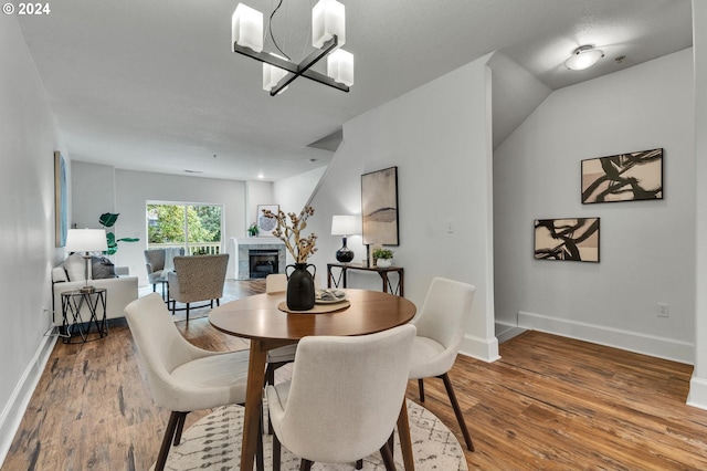 dining area with an inviting chandelier, hardwood / wood-style flooring, a fireplace, and vaulted ceiling