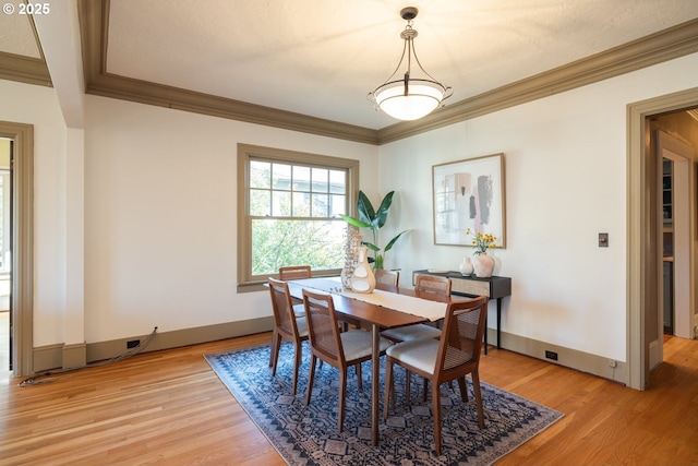 dining space with ornamental molding and light hardwood / wood-style flooring