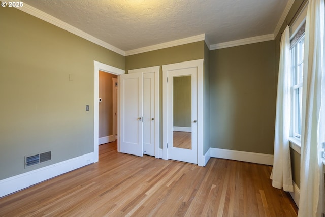 unfurnished bedroom featuring ornamental molding, a textured ceiling, and light wood-type flooring