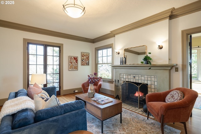 living room featuring a tile fireplace, ornamental molding, and light hardwood / wood-style flooring