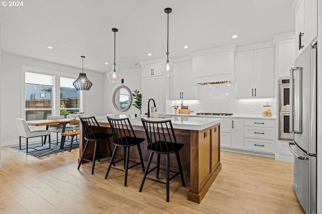 kitchen with sink, light hardwood / wood-style floors, a kitchen island with sink, and white cabinets