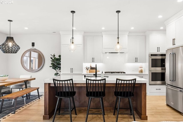 kitchen with a center island with sink, light hardwood / wood-style flooring, stainless steel appliances, pendant lighting, and a breakfast bar