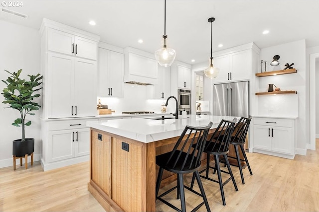 kitchen with light hardwood / wood-style flooring, a center island with sink, sink, white cabinets, and a breakfast bar area