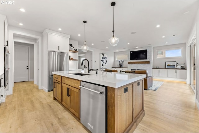 kitchen featuring light wood-type flooring, a center island with sink, appliances with stainless steel finishes, white cabinets, and sink