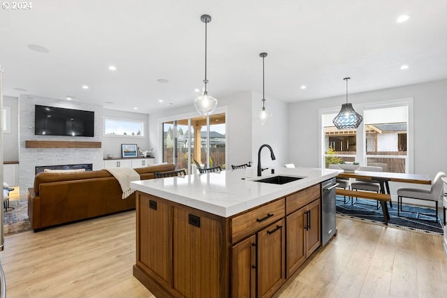 kitchen with plenty of natural light, light hardwood / wood-style floors, a fireplace, an island with sink, and sink