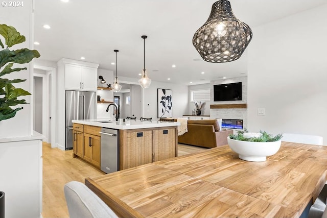 kitchen with light hardwood / wood-style floors, a center island with sink, a fireplace, white cabinets, and appliances with stainless steel finishes