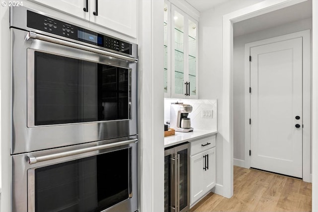 kitchen featuring light hardwood / wood-style floors, backsplash, wine cooler, white cabinets, and stainless steel double oven