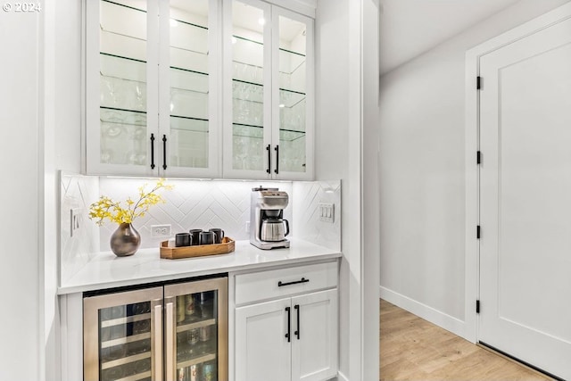 bar with wine cooler, white cabinets, tasteful backsplash, and light wood-type flooring