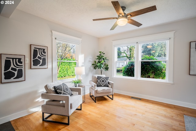 living area with ceiling fan, light wood-type flooring, and a textured ceiling