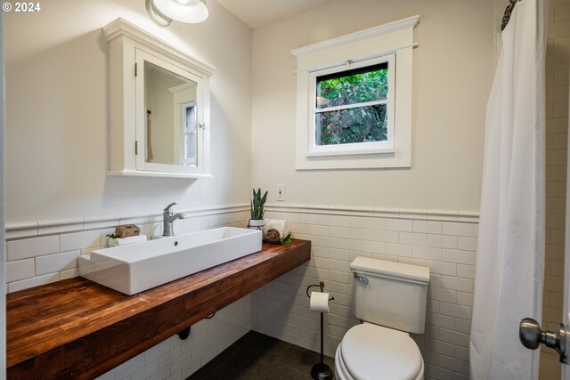 bathroom with tile patterned floors, toilet, sink, and tile walls