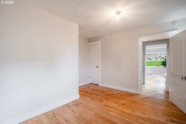 empty room with light wood-type flooring and a textured ceiling