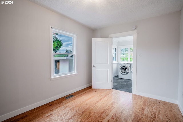 empty room with hardwood / wood-style floors, a textured ceiling, separate washer and dryer, and a healthy amount of sunlight